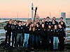 Gruppe unge mennesker poserer foran en rakett ved et kystnært oppskytingsområde.