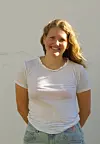 Smilende kvinne med hvit T-skjorte og jeans foran en lys vegg.