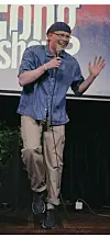 Ruben står på en scene med mikrofon, smiler og gestikulerer foran en projisert bakgrunn.