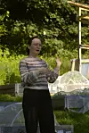 Anna Swiergon snakker i en frodig hage foran et veksthus og plantekasser.
