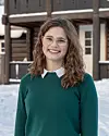Portrett av Tora Tveiten i grønn genser foran en snødekt trebygning.