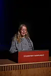 Kvinne taler ved en rød talerstol.